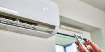 This stock image shows a person adjusting the temperature on an air conditioner.