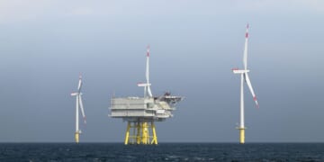 The photo presents a wide, horizontal view of the Borkum Riffgrund wind farm, where several wind turbines are erected in the open sea.