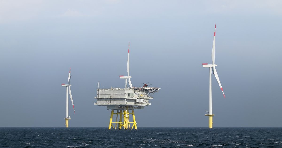 The photo presents a wide, horizontal view of the Borkum Riffgrund wind farm, where several wind turbines are erected in the open sea.