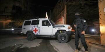 A gunman wearing the uniform of the al-Qassam Brigades, the military wing of Hamas, stands guard as Red Cross vehicles enter a warehouse allegedly to collect coffins containing the bodies of four deceased hostages in Gaza City on Tuesday.