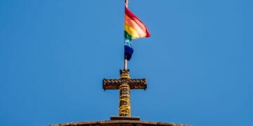 A pride flag stands on top of a Christian cross at a church.