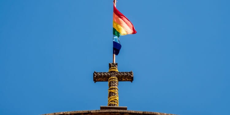 A pride flag stands on top of a Christian cross at a church.
