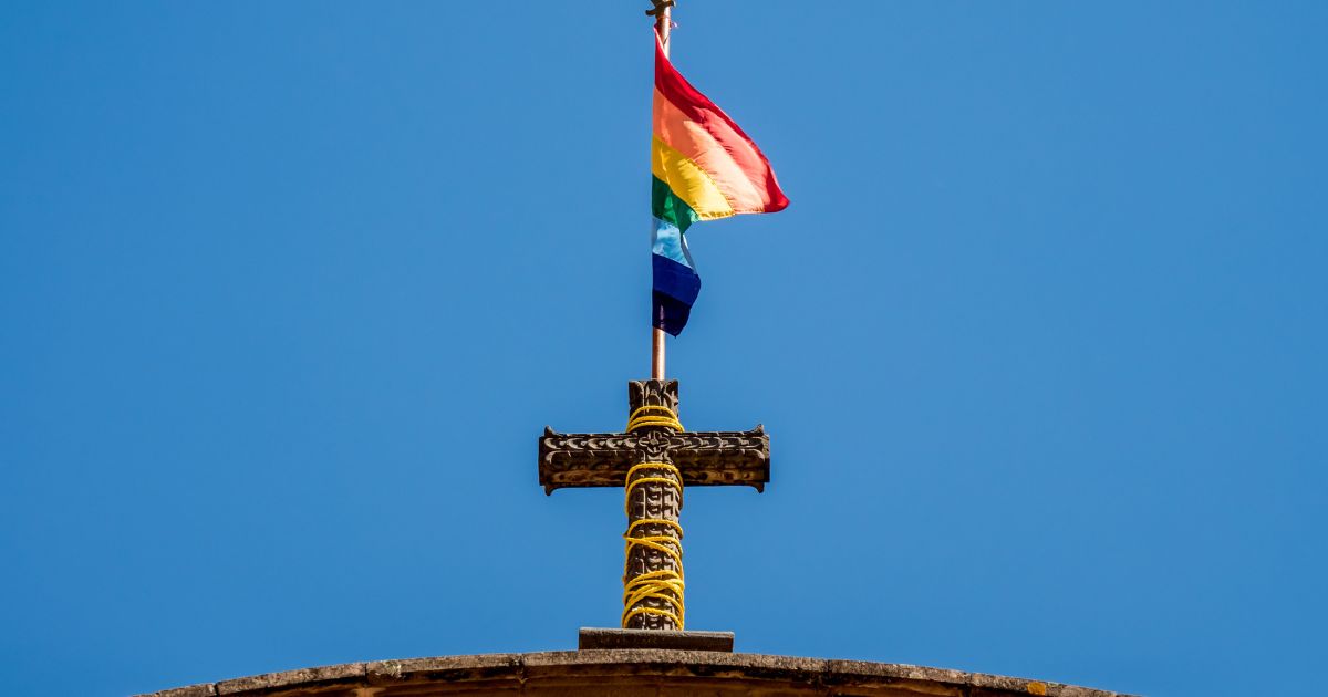 A pride flag stands on top of a Christian cross at a church.