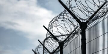 A prison border fence with razor wire against dark sky.