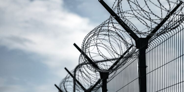 A prison border fence with razor wire against dark sky.