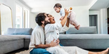 A husband and wife play with their daughter at home.