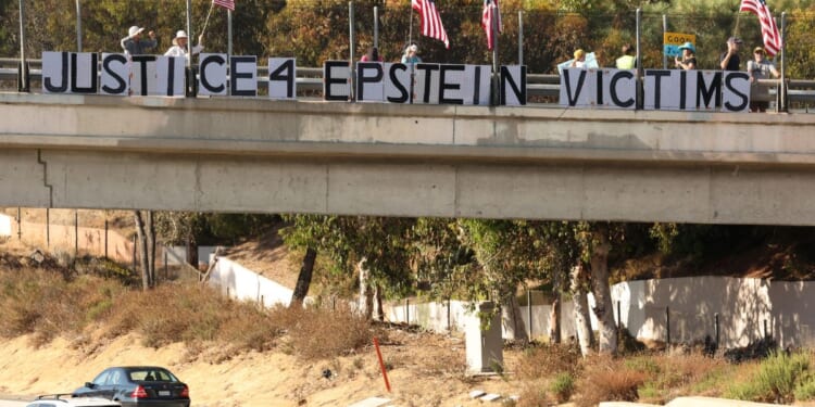 People hold American flags and signs reading "Justice 4 Epstein Victims" on a freeway overpass in Encinitas, California, on July 31, 2025.