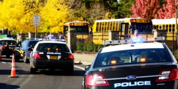 Police cars are parked near the entrance of a High School.