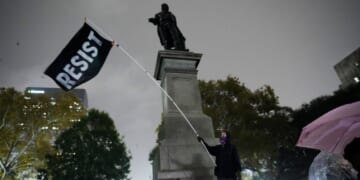 A protestor waves a flag in a pouring rain during a demonstration against an impending Customs and Border Patrol immigration crackdown in New Orleans on Dec. 1, 2025.