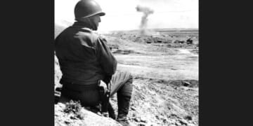 American military commander Lieutenant General George S. Patton (1885 - 1945) sits on the sand and watches a tank battle in Tunisia, 1943.