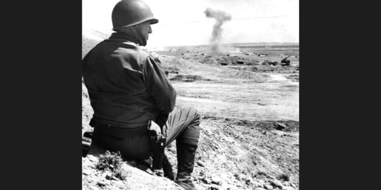 American military commander Lieutenant General George S. Patton (1885 - 1945) sits on the sand and watches a tank battle in Tunisia, 1943.