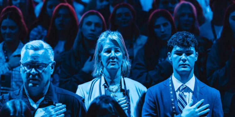 Attendees stand for the National Anthem during Turning Point's annual AmericaFest conference in Phoenix, Arizona, on Dec. 21, 2025.