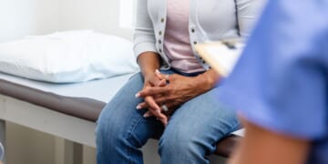 A woman clasps her hands during a discussion with medical personnel.