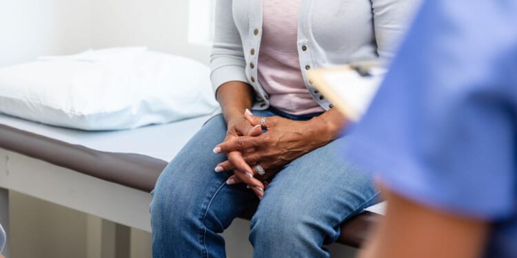 A woman clasps her hands during a discussion with medical personnel.