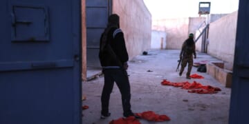 Syrian government fighters walk inside Al-Shaddadi prison, where red detainee suits lie on the ground, in the town of Shaddadeh, northeastern Syria, on Tuesday, a day after Syria's Interior Ministry said Islamic State group members escaped from the facility during clashes with the Kurdish-led Syrian Democratic Forces.