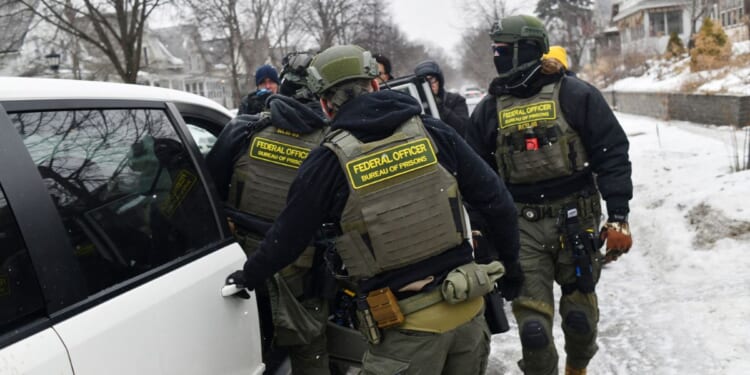 Federal agents return to their car after a patrol in the Frogtown neighborhood while anti-ICE activists warn the community about their presence and oppose ongoing Immigration and Customs Enforcement detentions, part of heightened tensions following a federal immigration enforcement surge and recent shooting involving an ICE officer in St. Paul, Minnesota, on Jan. 16, 2026.