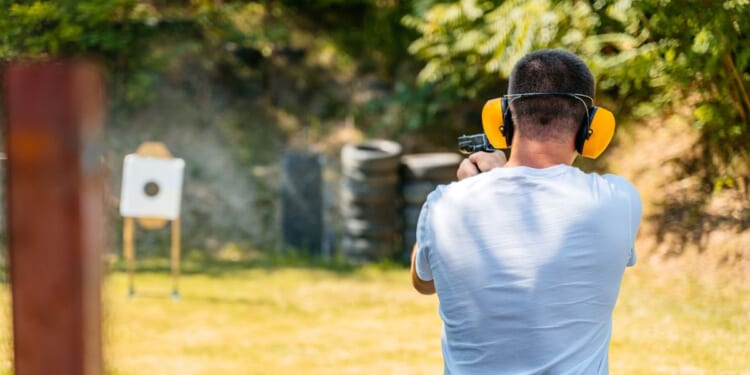 Adult man shooting a target with a handgun in an outdoor shooting range.