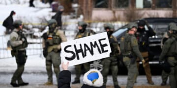 An onlooker holds a sign that reads "Shame" as members of law enforcement work the scene following a suspected shooting by an ICE agent during federal law enforcement operations on Jan. 7, 2026, in Minneapolis, Minnesota.