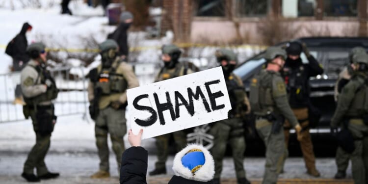 An onlooker holds a sign that reads "Shame" as members of law enforcement work the scene following a suspected shooting by an ICE agent during federal law enforcement operations on Jan. 7, 2026, in Minneapolis, Minnesota.
