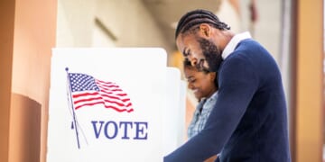 A young man and woman voting at a voting booth in a US election.