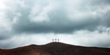 Three crosses line the top of a barren gloomy hill.