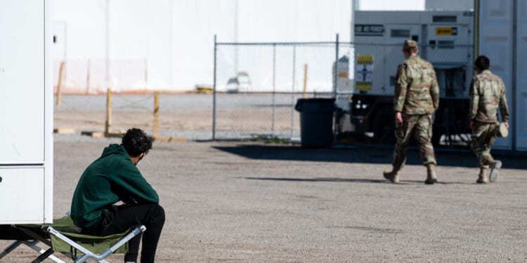 An Afghan refugee sits and watches as U.S. military service members pass in an Afghan refugee camp on Nov. 4, 2021, in Holloman Air Force Base, New Mexico.