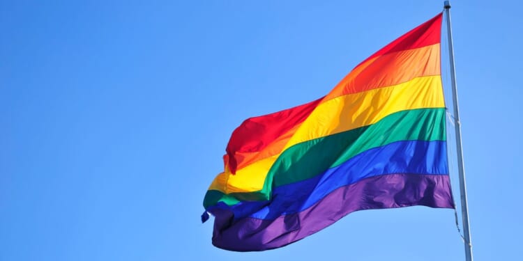 A rainbow "pride" flag waves in front of a blue sky.