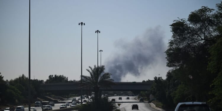Motorists drive along a street as smoke rises from a reported Iranian strike in the area where the U.S. Embassy is located in Kuwait City on March 2, 2026.