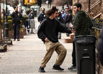 A left-wing activist is handed a homemade explosive device by a fellow activist before throwing it toward police during an anti-Islamic protest Saturday in front of Gracie Mansion, New York mayor Zohran Mamdani's official residence.