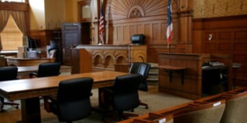 An empty, brown-paneled courtroom with flags.