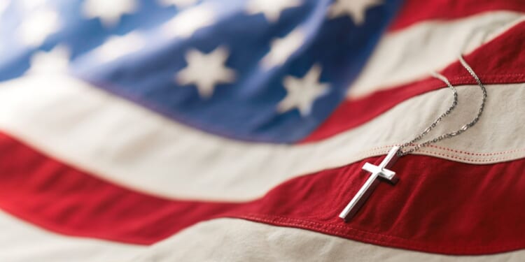A Christian cross neckless is laid across an American flag.