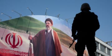 A member of the Iranian security forces stands guard under a large portrait of Iran's new Supreme Leader, Mojtaba Khamenei, during a memorial to mark the 40th day since his father, Ali Khamenei, was killed in U.S.-Israeli joint strikes on April 9, 2026, in Tehran, Iran.