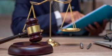 A person sits at a desk analyzing files as the weights of Justice stand and a gavel sits.