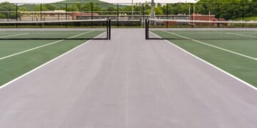A new green tennis court with white lines and gray outside of the play area.