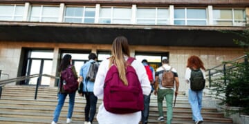 Students walk up the steps of a schoolhouse.