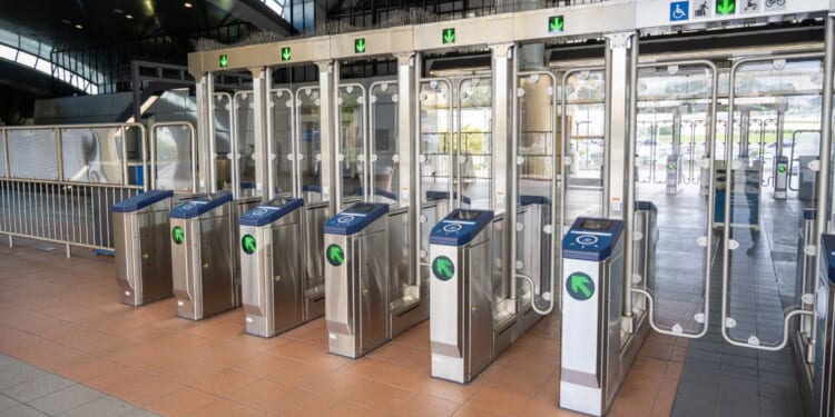 Row of stainless steel fare gates with glass barriers and accessibility icons ar seen Oct. 15 at the BART transit station entrance in South San Francisco, California.