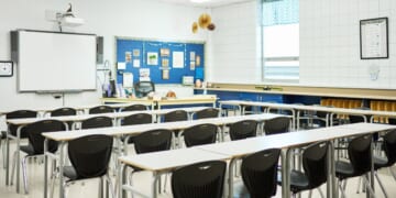 Chairs and desks sitting in rows in front of a whiteboard in a school classroom with no students.