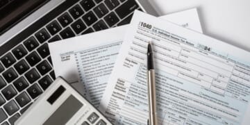 Papers and calculating tools are thrown across a desk.
