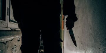 A murderer holds a bloodstained knife.