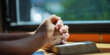 Hands in a prayerful position placed on a Bible.