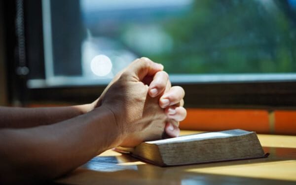 Hands in a prayerful position placed on a Bible.