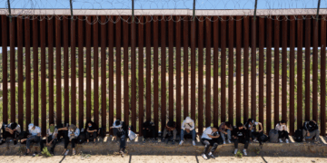 Migrants sit by the iron fence waiting to be processed by the U.S. Border Patrol near the Jacumba Hot Springs after crossing the border.